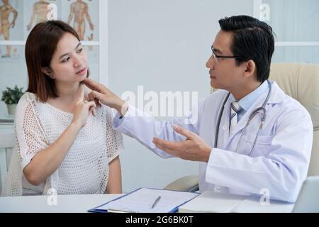 Arzt berührt den Hals einer jungen Frau, die an chronischen Schmerzen leidet Stockfoto