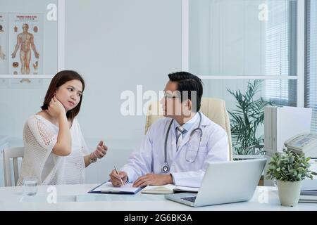 Eine junge Frau beschwert sich über Schmerzen im Nacken, als sie mit einer Allgemeinpraktizierenden spricht Stockfoto