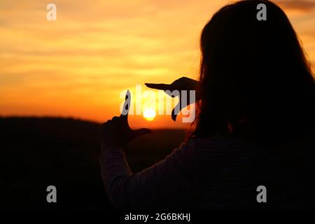 Hintergrundbeleuchtetes Porträt einer Frau Hände Silhouette Rahmen Sonne bei Sonnenuntergang Stockfoto