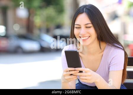 Asiatische Frau mit Smartphone auf einer Bank auf der Straße sitzen Stockfoto