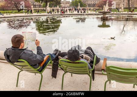 Zwei Touristen, die in ihren Stühlen schaukeln, sitzen am Rande eines Wasserkörpers im Garten der Tuilerien in Paris Stockfoto
