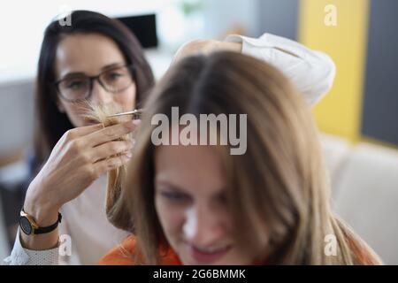 Junge Frau schneidet ihre Haarspitzen mit einer Schere zu ihrem Freund zu Hause Nahaufnahme Stockfoto