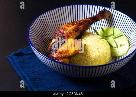 Food-Konzept Röstliches Hühnchen-Qaurter und Kurkuma-Reis auf schwarzem Hintergrund mit Kopierfläche Stockfoto