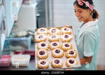 Eine junge Inhaberin eines kleinen Unternehmens ist leidenschaftlich über ihre handgemachten leckeren Donuts von unwiderstehlichem Aussehen. Gebäck, Dessert, süß, Zubereitung Stockfoto