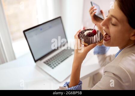 Eine junge Geschäftsfrau isst mit Vergnügen einen leckeren Donut, während sie in angenehmer Atmosphäre in einer Konditorei Freizeit verbringt. Konditorei de Stockfoto