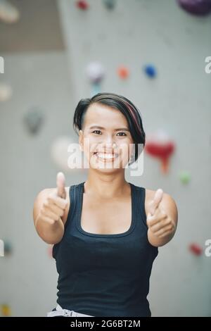 Porträt einer lächelnden, jungen Frau mit Daumen nach oben, wenn sie im Kletterzentrum steht Stockfoto