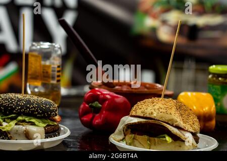 Zwei Käseburger auf einem Tisch mit roten und gelben Paprika im Hintergrund an der Lebensmitteltheke Stockfoto