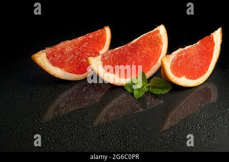 Grapefruitscheiben auf dunklem Grund mit einem Minzzweig. Isolieren. Speicherplatz kopieren. Stockfoto
