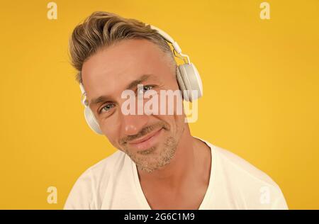 Hören Sie genau zu. Mann mittleren Alters trägt Kopfhörer auf gelbem Hintergrund. Englische Schule. Fremdsprache lernen. Audiokurse. Zuhören Stockfoto