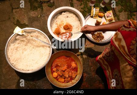 Eine Frau kocht Biryani. Biryani ist ein indo-arisches Wort, das vom persischen Wort „Birian“ abgeleitet wurde, was ‘vor dem Kochen gebraten’ und „Birinj“, das persische Wort für Reis, bedeutet. Die Biryani ist eines der beliebtesten und bestellten Gerichte in Indien. Es wird mit indischen Gewürzen, Reis und Fleisch (Huhn, Rindfleisch, Ziege, Lamm, Garnelen, Fisch), und manchmal, zusätzlich, Eier oder Gemüse wie Kartoffeln in bestimmten regionalen Sorten. Es gibt verschiedene Theorien über die Herkunft dieses leckeren Gerichts. Viele Historiker glauben, dass Biryani aus Persien stammte und von den Moguln nach Indien gebracht wurde. Stockfoto