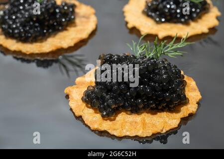 Schwarzer Kaviar in Tartlets auf dunklem Hintergrund. Gesundes Lebensmittelkonzept. Speicherplatz kopieren. Stockfoto