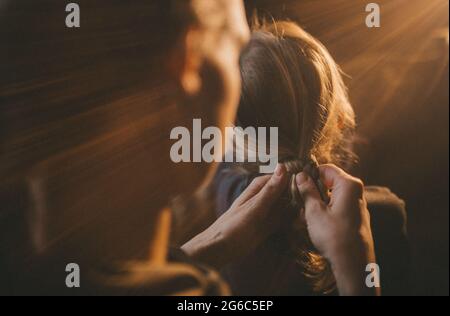 Mutter flechtert die Haare ihrer Tochter. Stockfoto