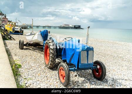 Blick auf Traktor und Fischerboot am Strand von Cromer im Norden von Norfolk, Großbritannien, mit berühmtem Pier im Hintergrund Stockfoto