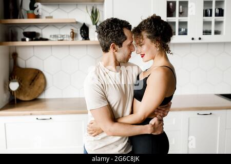 Glückliche Millennial Ehemann und Ehefrau umarmen Kuscheln und genießen romantischen Moment in der modernen Küche, liebevolle junge Paar umarmen zu Hause, einander in die Augen schauen Stockfoto