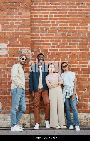 Ganzjährige Ansicht auf verschiedene Gruppen junger Menschen, die im Freien posieren und die Kamera betrachten, während sie an einer Ziegelwand in einer städtischen Umgebung stehen und den Raum kopieren Stockfoto