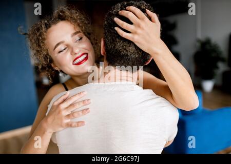 Junger, liebevoller Mann umarmt und umarmt lächelnde kaukasische Frau während eines leidenschaftlichen romantischen Moments zu Hause. Glückliche Familie zartes Paar mit Spaß Stockfoto