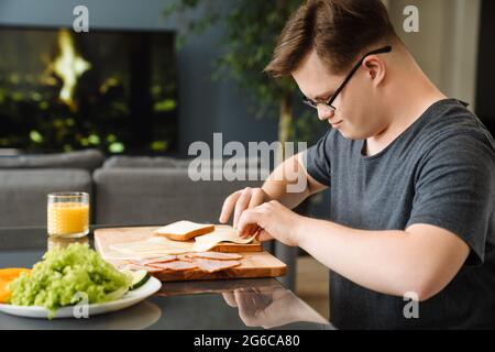 Junger Mann mit Down-Syndrom macht Sandwiches in der Küche zu Hause Stockfoto