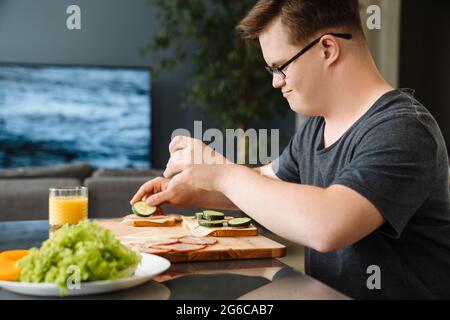Junger Mann mit Down-Syndrom macht Sandwiches in der Küche zu Hause Stockfoto