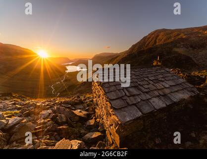 Warnscale Bothy Sonnenuntergang mit einem großen Sonnenstrahl, der über die Bergkamm-Linie hereinkommt und in Richtung Buttermere Lake blickt. Stockfoto