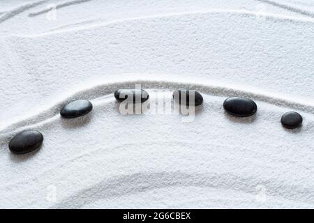 Zen schwarze Kieselsteine auf weißem Sand Stockfoto