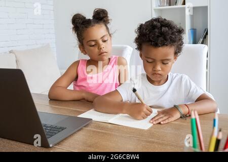 afroamerikanische ältere Schwester, die dem jüngeren Bruder bei Hausaufgaben am Schreibtisch zusieht Stockfoto
