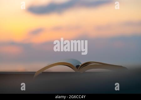 Verbringen Sie einen schönen Abend beim Lesen eines interessanten Buches im Freien bei mildem Sonnenuntergang. Halten Sie einen Stift, um die wichtigsten Dinge zu markieren. Ruhige Angenehme Zeitvertreib. Stockfoto