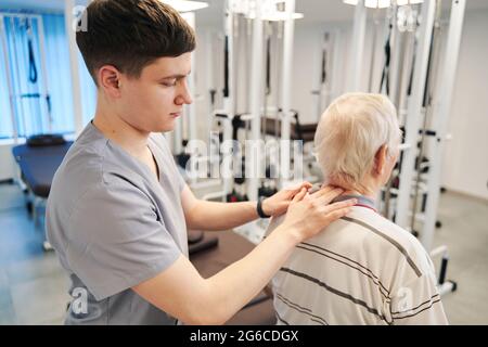 Junge Physiotherapeutin drückt mit zwei Fingern auf den Rentnerhals Stockfoto