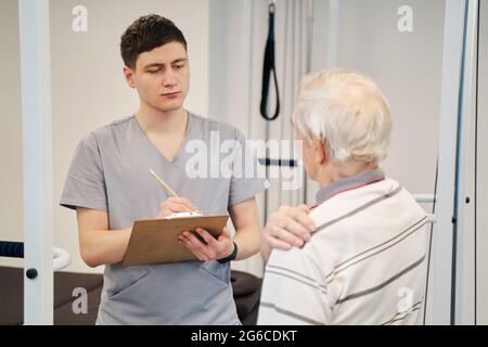 Aufmerksamer Physiotherapeut, der in seinem Notizbuch über Patientenbeschwerden schreibt Stockfoto