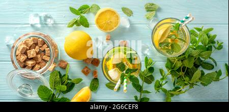 Sommerliche kalte Getränke in Gläsern mit Zitronen, Minzen auf blauem Holzhintergrund. Draufsicht auf Limonade mit Rohrzucker und Papierhalmen für Getränke. Stockfoto