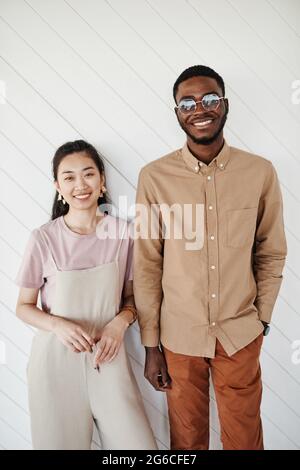 Portrait eines modernen Mischvolkspaares, das an einer weißen Wand posiert und die Kamera anlächelt Stockfoto