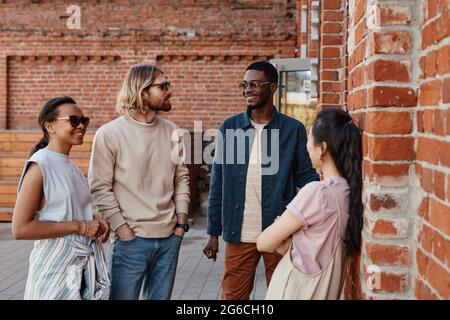 Eine vielfältige Gruppe junger Menschen, die im Freien plaudern, während sie an einer Backsteinmauer in einer städtischen Umgebung stehen und Raum kopieren Stockfoto