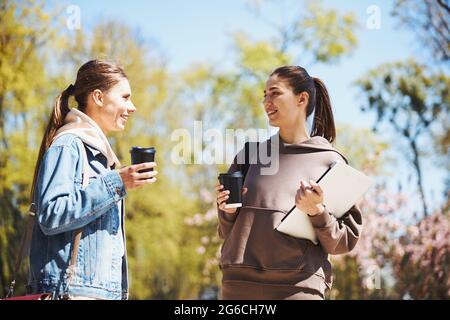 Zwei Frauen unterhalten sich, während sie Kaffeetassen halten Stockfoto
