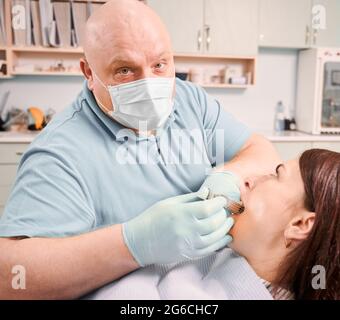 Nahaufnahme von männlichen Zahnarzt in medizinischen Gesichtsmaske und sterile Handschuhe Durchführung zahnärztliche Verfahren in modernen medizinischen Zentrum. Konzept der Zahnmedizin, Stomatologie und Zahnpflege. Stockfoto