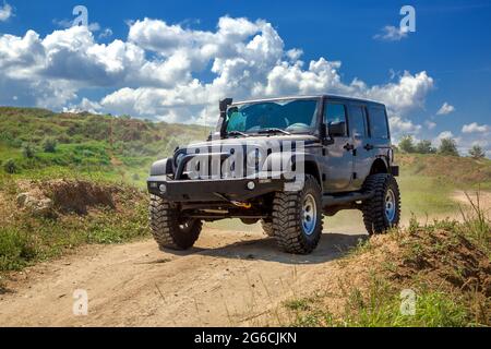 Schwarzes SUV-Auto mit Winde und großen Rädern für Offroad-Fahrten auf einem rauen Trail auf Lehm hügeligen Landschaften mit Hängen an einem sonnigen Tag mit cl Stockfoto