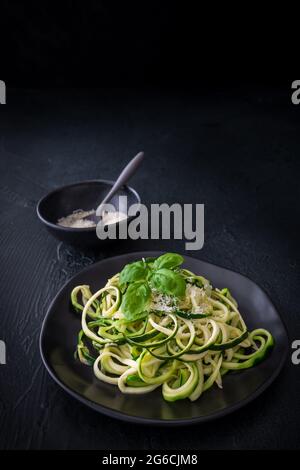 Zoodles, Zucchini-Nudeln mit Parmesan und Basilikum auf einem schwarzen Teller auf schwarzem Hintergrund. Für Low Carb, Keto, Vegetarier, Paläo Ernährung und Ernährung. Version Stockfoto