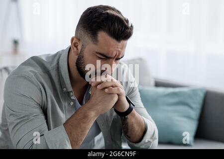 Unglücklich depressiv kaukasisch schöner bärtiger Mann weinte auf der Wohnzimmercouch und fühlte sich verzweifelt Stockfoto