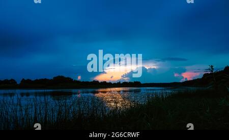 Schöner, magischer Sonnenuntergang über dem See mit lockigen Wolken im Sommer und der Reflexion des Lichts auf dem Wasser Stockfoto