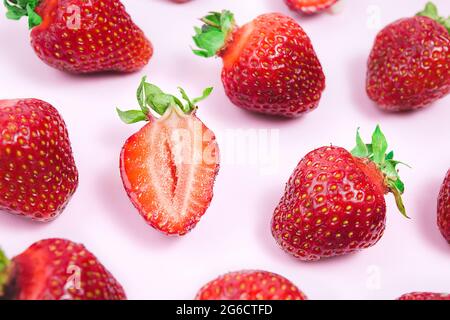 Erdbeer-Kreativmuster. In Scheiben geschnittene reife rote Beere und ganze Erdbeeren mit grünen Blättern auf rosa Hintergrund. Stockfoto