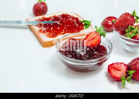 Hausgemachte Erdbeermarmelade oder Erdbeergelee mit frisch reifen Erdbeeren auf einem weißen Teller. Frühstück mit Brot Toast mit Erdbeermarmelade. Messer für s Stockfoto