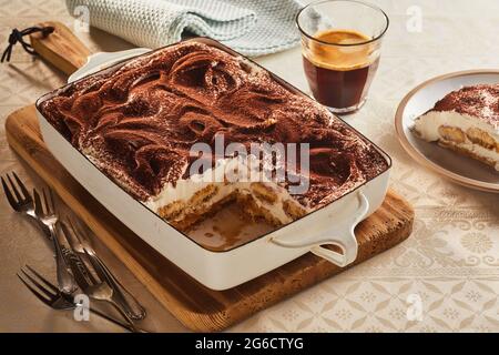 Hoher Winkel von leckeren traditionellen Tiramisu Kuchen in der Pfanne serviert auf dem Tisch mit einem Glas heißen Kaffee Stockfoto