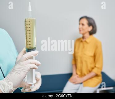 Spritze mit medizinischer Lösung in der Hand des Arztes, bevor der Arzt die Ohrenbewässerung durchführt, um Ohrenwachsansammlungen vom Patienten zu entfernen, die zu Hörverlust führen können Stockfoto