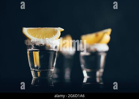 Tequila Schüsse mit Salz und Zitrone auf reflektierende Oberfläche vor dunklem Hintergrund platziert Stockfoto