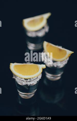 Tequila Schüsse mit Salz und Zitrone auf reflektierende Oberfläche vor dunklem Hintergrund platziert Stockfoto