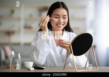 Schöne asiatische Dame mit Augenserum und lächelnd Stockfoto
