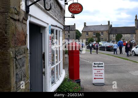 Touristen gehen an einem Teestube und einem Postgeschäft mit altmodischem roten Briefkasten im Dorf Peak District vorbei - Hartington, Derbyshire, England, Großbritannien Stockfoto