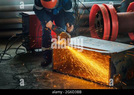 Ein Arbeiter schneidet Metall mit einem Handschleifer in der Produktionshalle und es fliegen leuchtende Funken. Eine echte Arbeitsumgebung. Ein Mann bei der Arbeit. Stockfoto