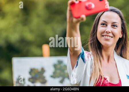 Junge Frau, die im Freien ein Selfie vor einer bemalten Leinwand gemacht hat Stockfoto