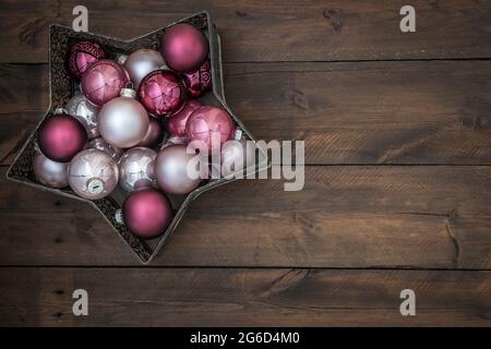 Sternförmige Schale gefüllt mit rosa und silbernen weihnachtskugeln. Auf Holzhintergrund mit Kopierraum. Stockfoto