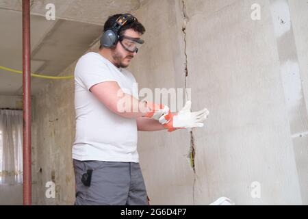 Der Baumeister legt Schutzhandschuhe an, trägt eine Schutzbrille und einen Gehörschutz. Sicherheit am Arbeitsplatz. Stockfoto