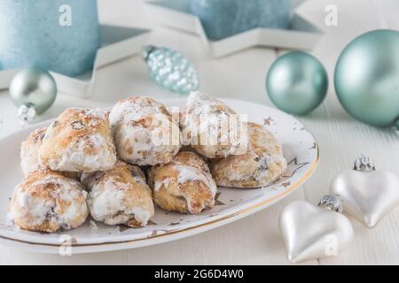 Süßer Mini-Stollen auf einem weihnachtlichen Teller auf einem weißen Holztisch, geschmückt mit schimmernden hellgrünen Kerzen und weihnachtskugeln und Herzen Stockfoto